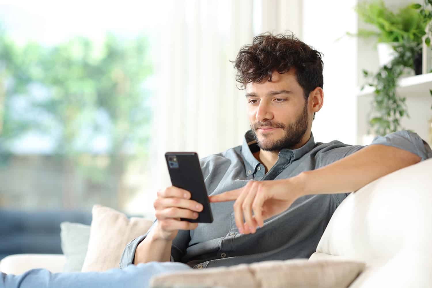 Man scrolling through his phone while sat on the couch.