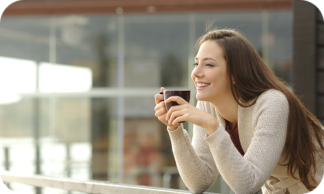 Woman looking from a balcony with a mug in her hands.